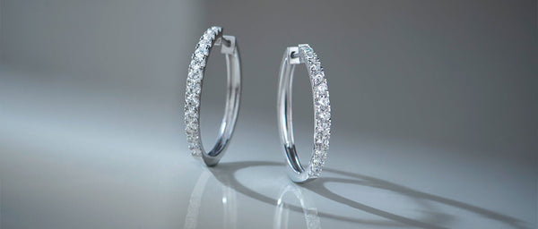 Pair of silver hoop earrings on a reflective surface with a gray background