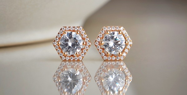 Hexagonal diamond earrings with rose gold accents on a reflective surface.