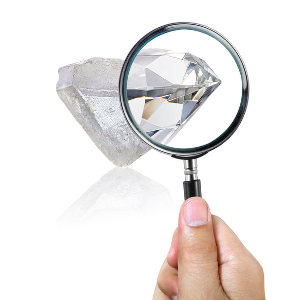 Hand holding a magnifying glass over a diamond on a white background