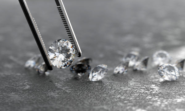 Diamonds being held by tweezers on a dark surface